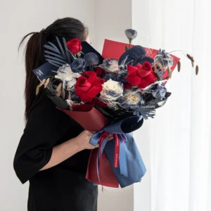 Midnight Charm Bouquet, a young lady holds a flower bouquet in red and blue wrapping with red rose, white on white florist, brithday bouquet for girlfriend