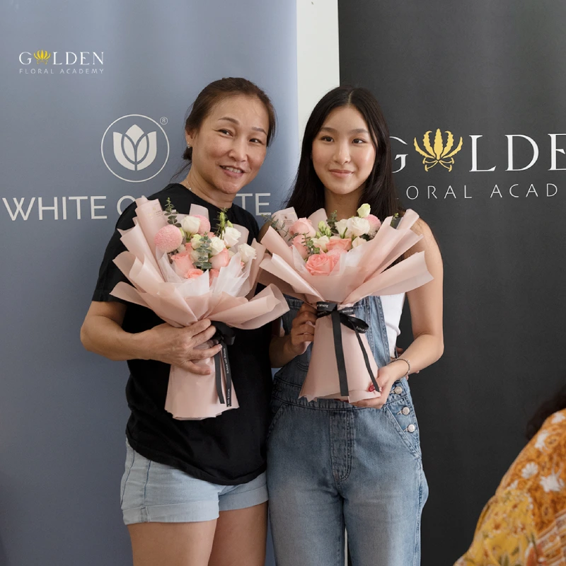 Asian mom and daughter smiling while holding pink flower bouquet, flower arrangement class