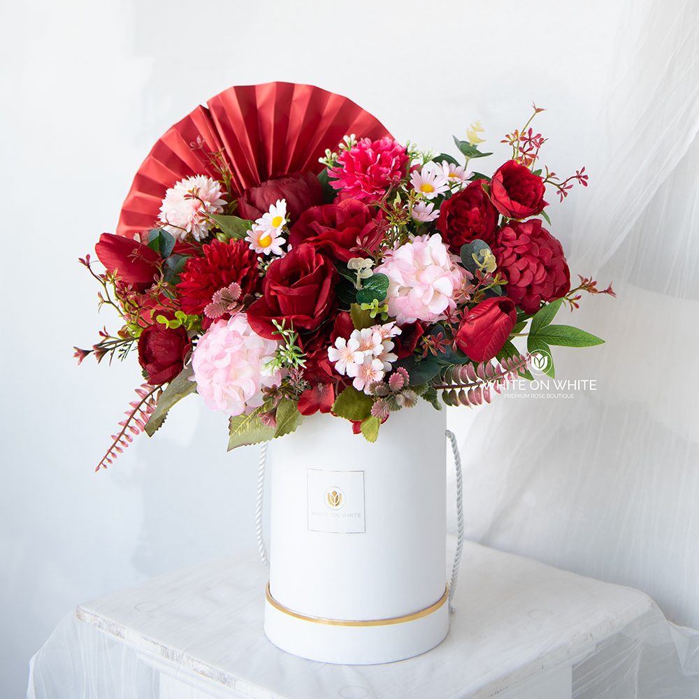 Red artificial flower arrangement in a white box