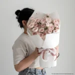 Pink and cream rose bouquet wrapped in white paper, held by a woman.